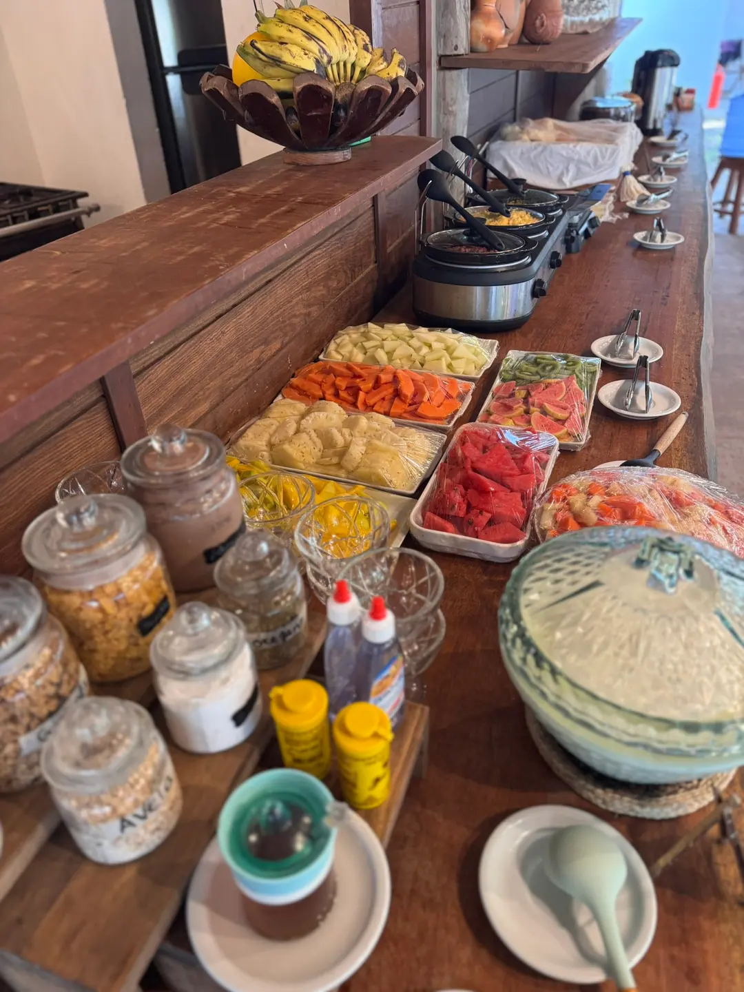 Mesa do café da manhã da pousada, com frutas, tapioca e pães