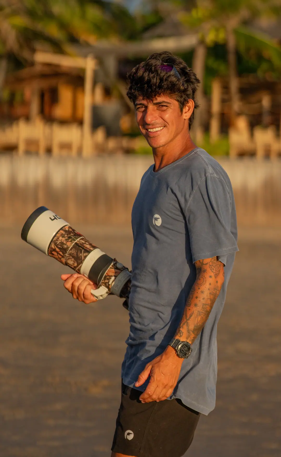 Photographer Caio Florentino on Atins beach, smiling, with his camera and a telephoto lens, at sunset