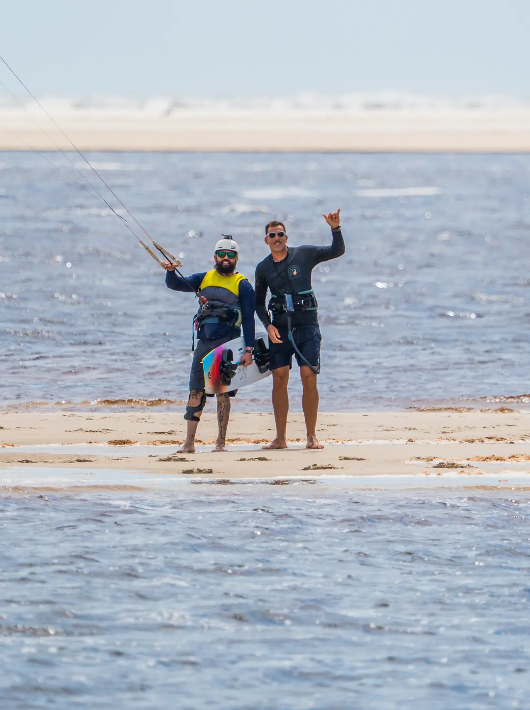 Duas pessoas acenando na água, com a prancha de kite