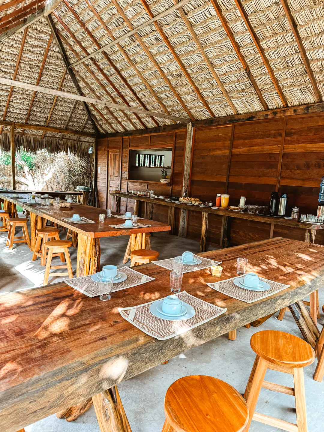 O restaurante da pousada, com mesas de madeira sob o telhado de palha